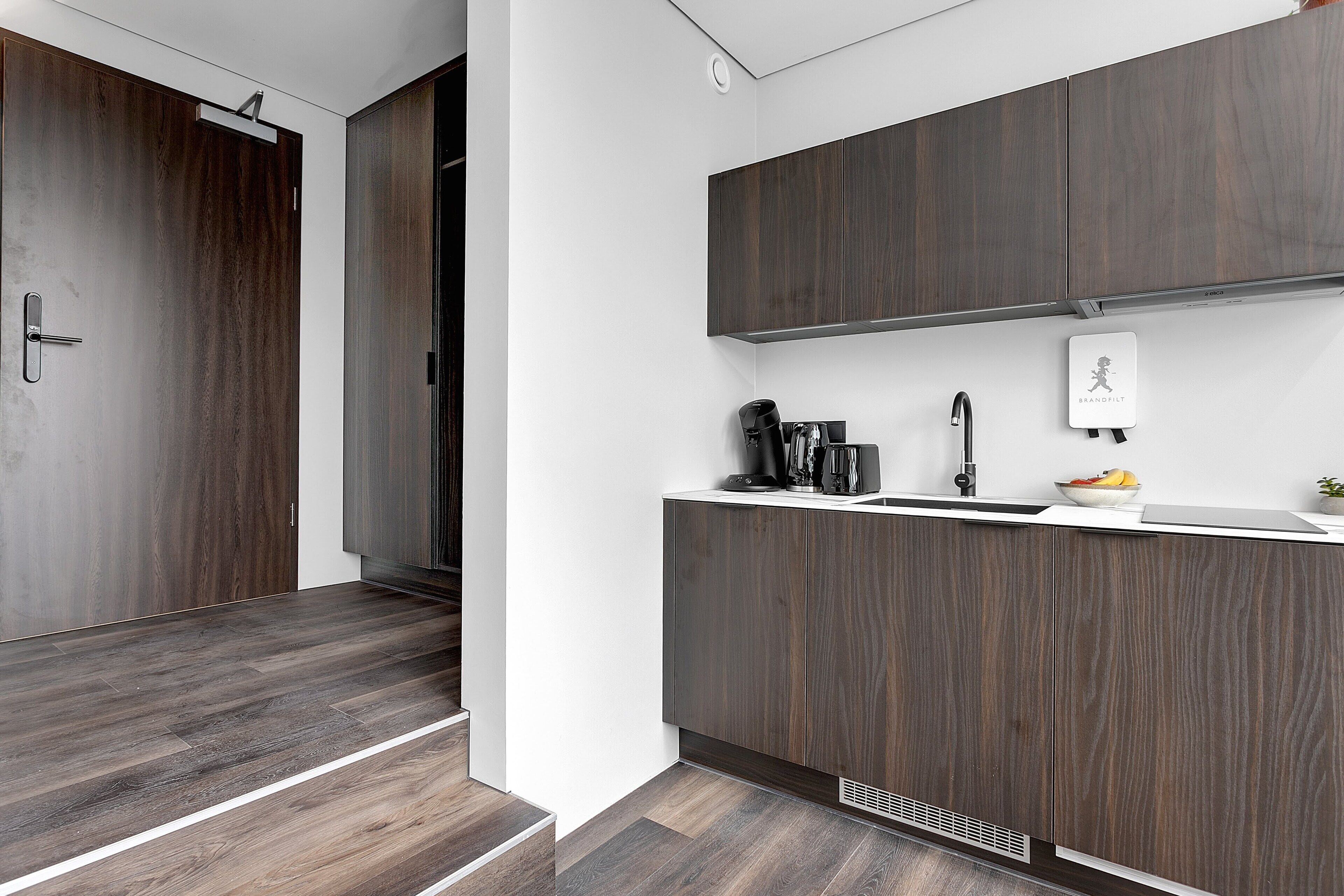 Une cuisine moderne avec des meubles de couleur bois foncé, un plan de travail blanc et une hotte intégrée.