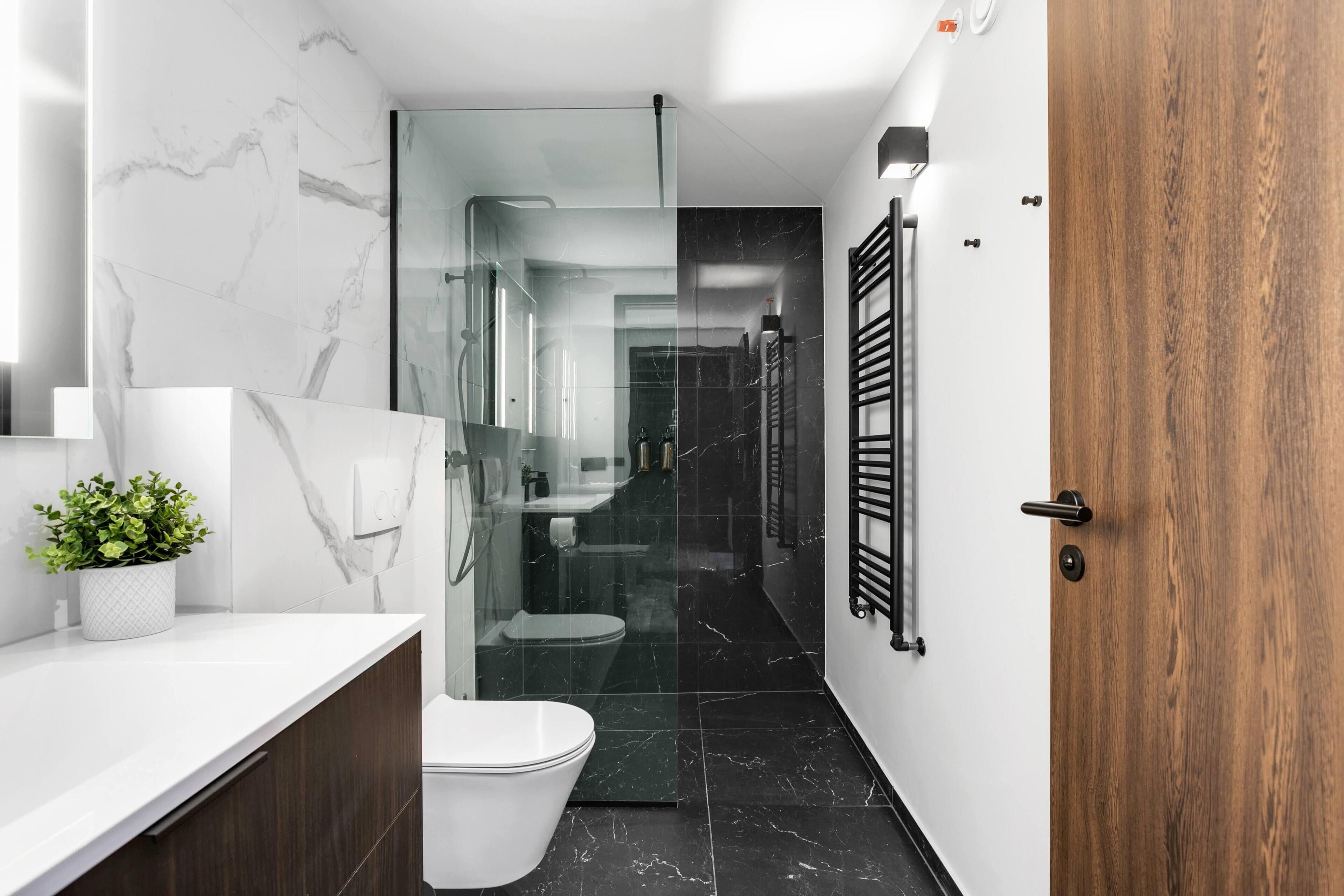 A modern bathroom with a white toilet, a glass shower enclosure, and a wooden door.