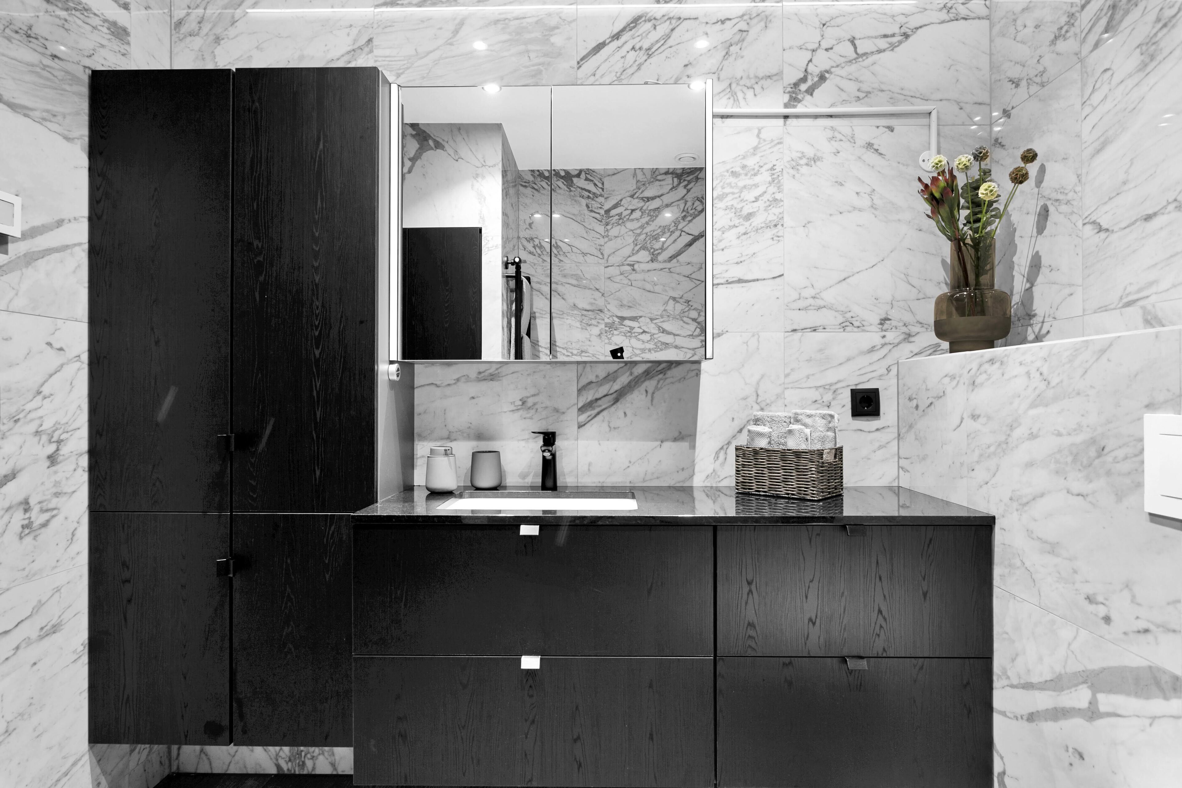 A modern bathroom with a dark wooden vanity, a large mirror, and a marble backsplash.