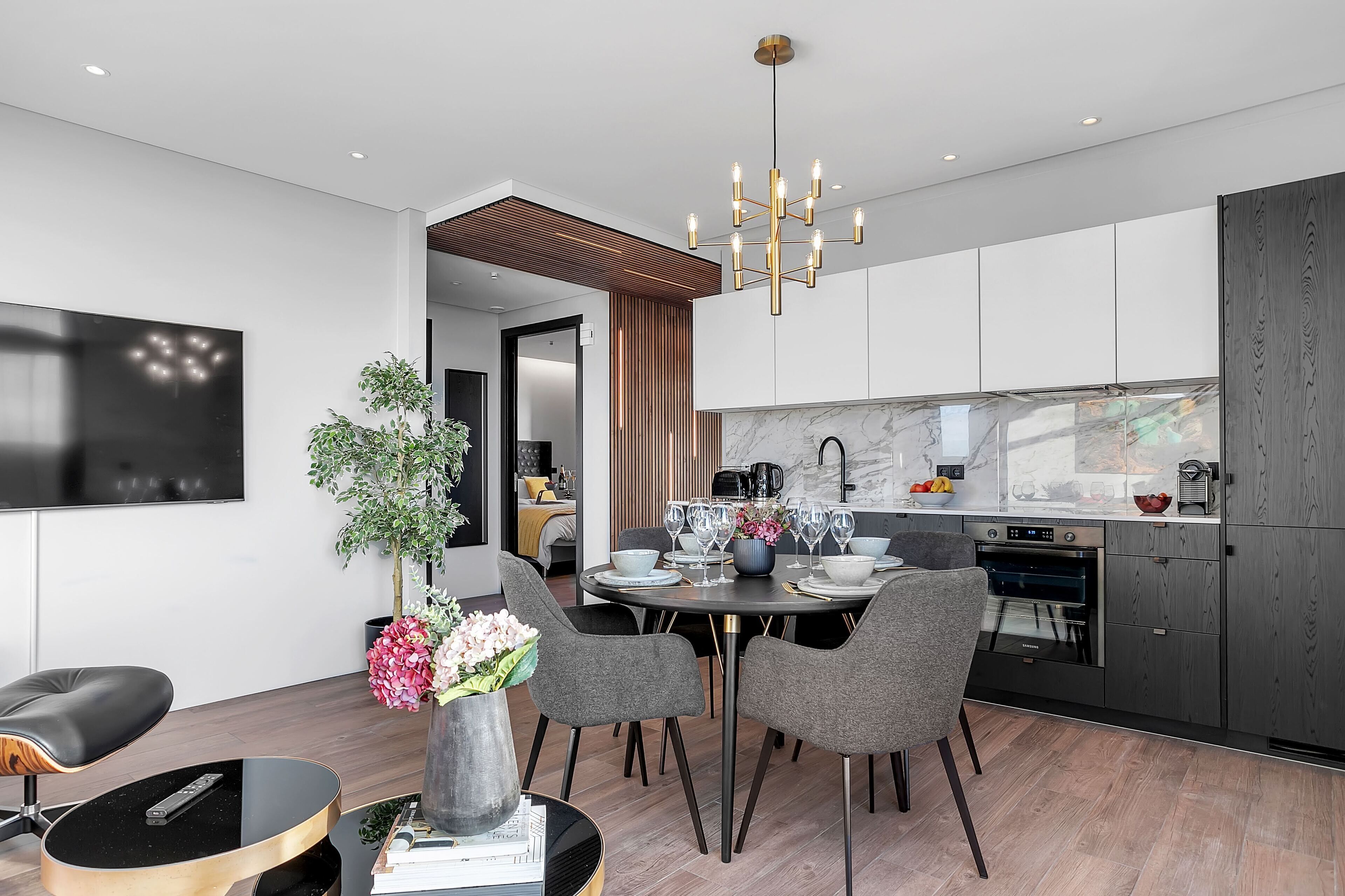 A modern kitchen with a built-in oven, a dining area with a round table, and a TV mounted on the wall.