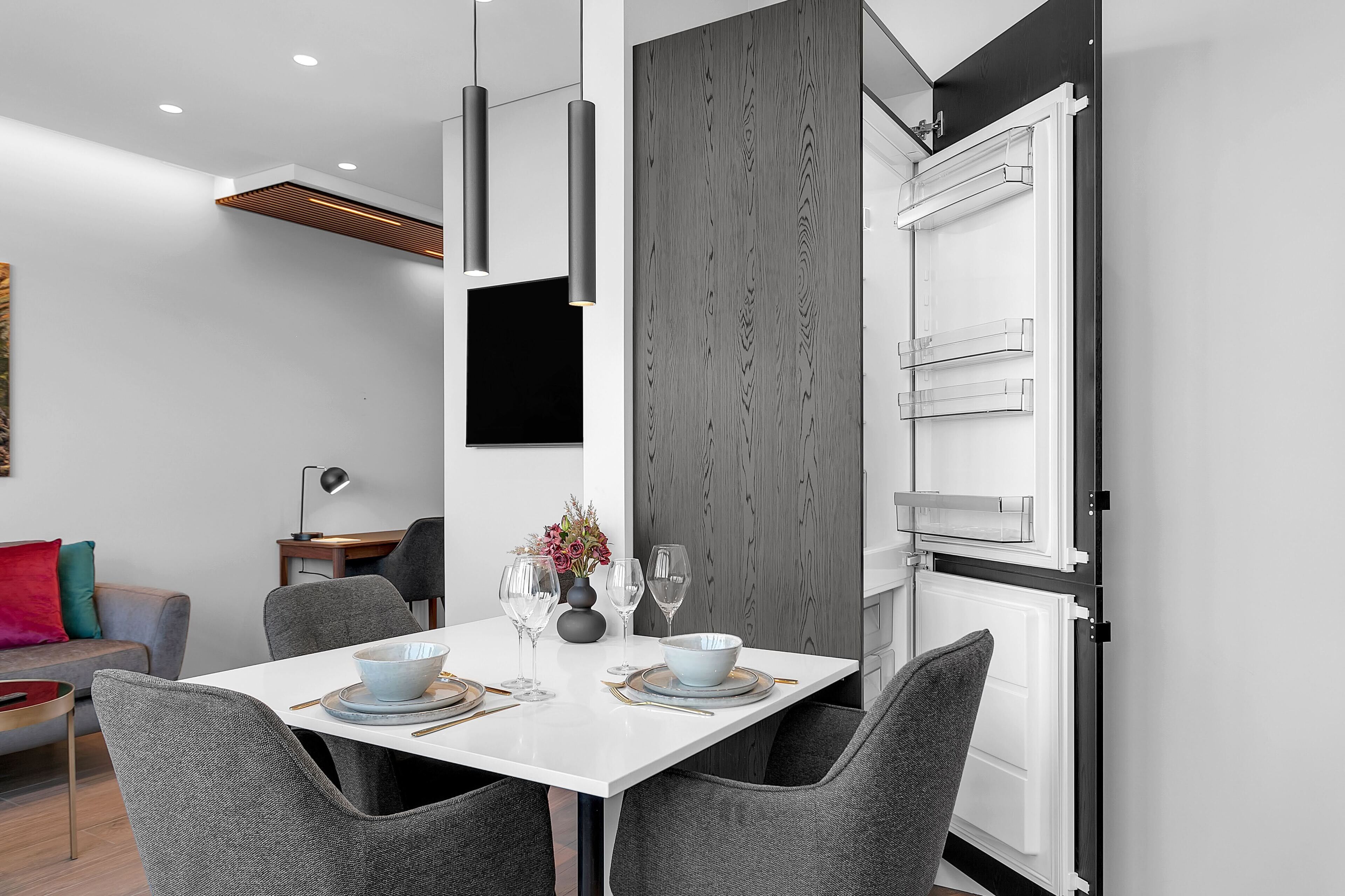 A modern dining area with a white table, grey chairs, and a built-in white cabinet with a grey wood panel.