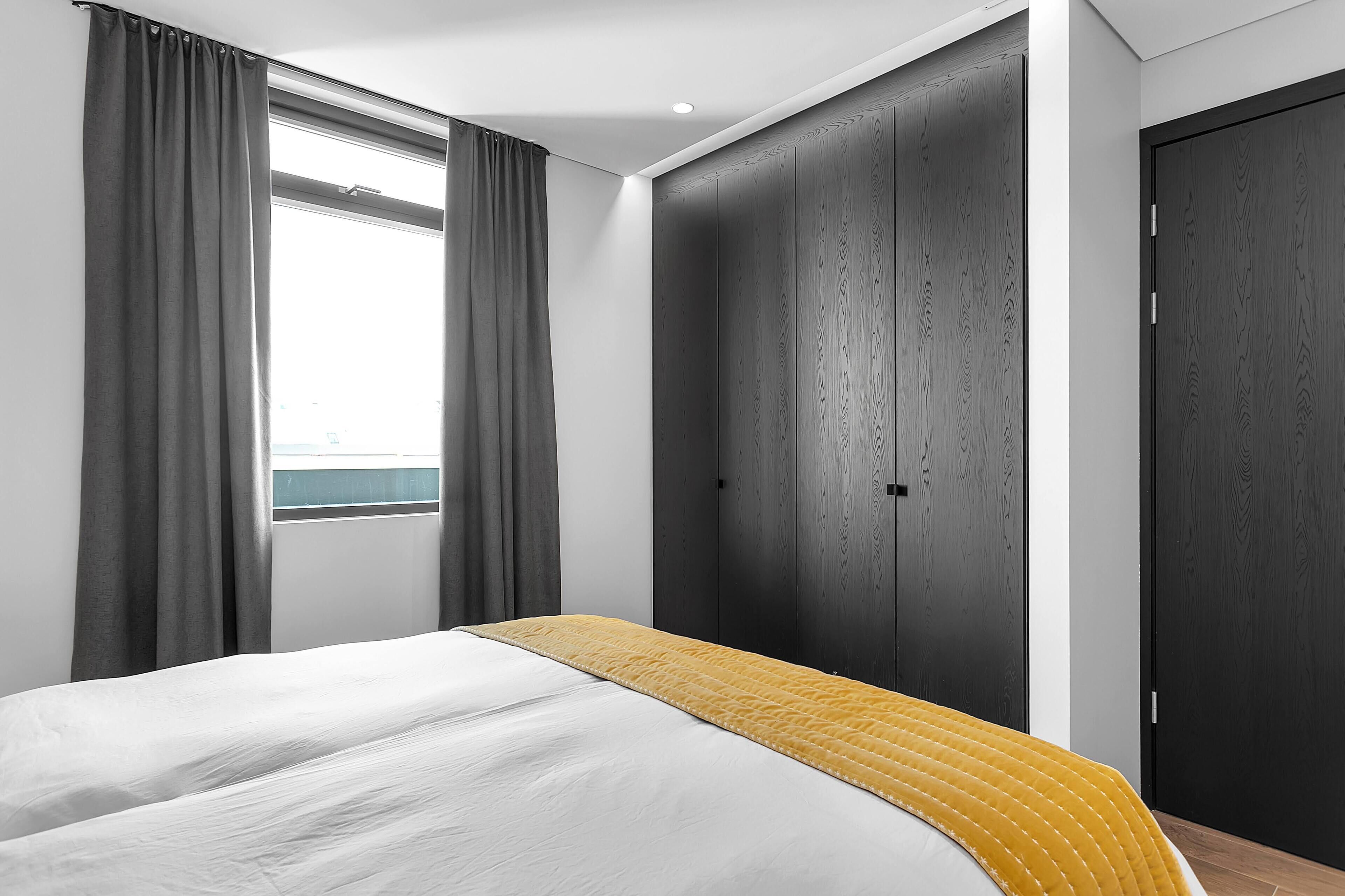 Ein Schlafzimmer mit Bett, einem Fenster mit Vorhängen, einem Kleiderschrank und einer Tür.