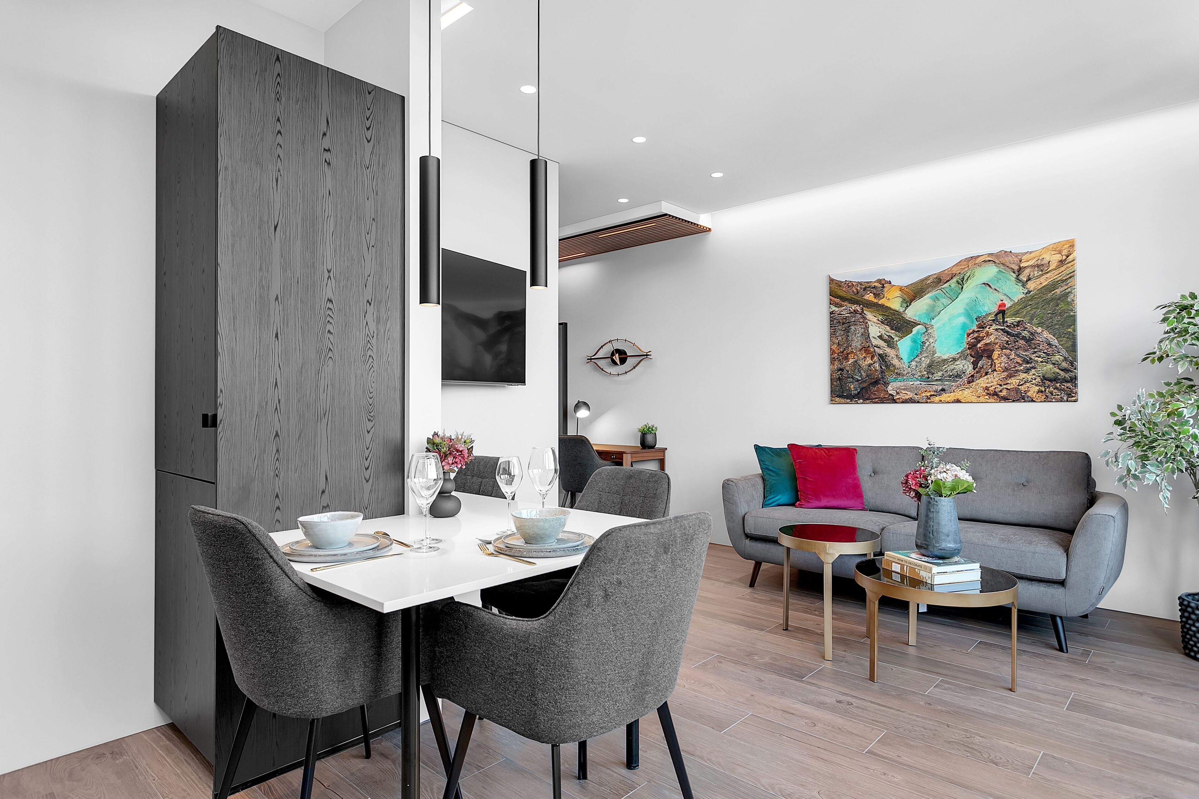 Un salon moderne comprenant un coin repas, des fauteuils à revêtement gris, une table blanche et un canapé gris agrémenté de coussins colorés.