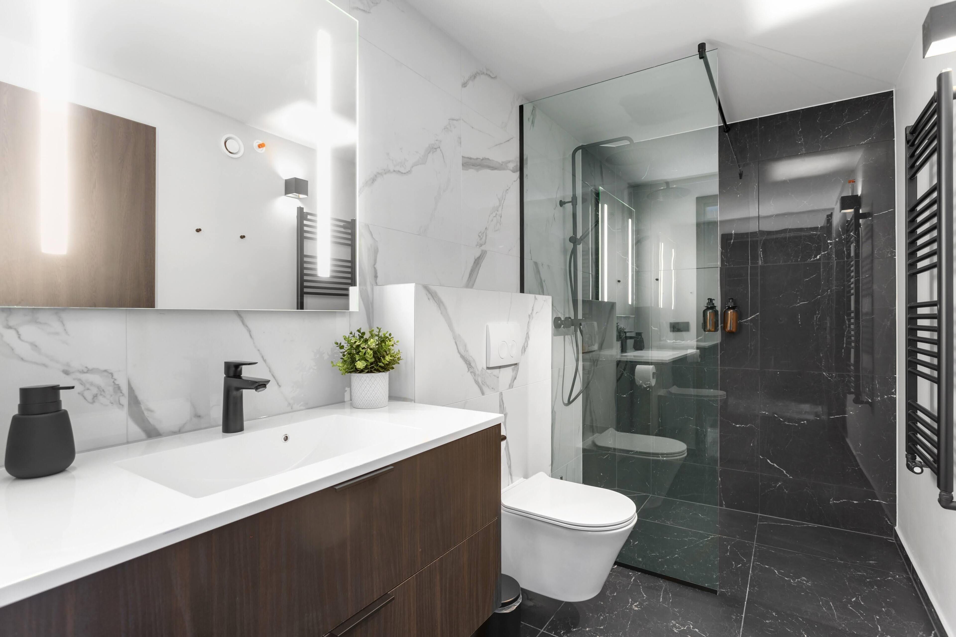 A modern bathroom with a marble sink, dark wood vanity, a white toilet, and a glass-enclosed shower area.