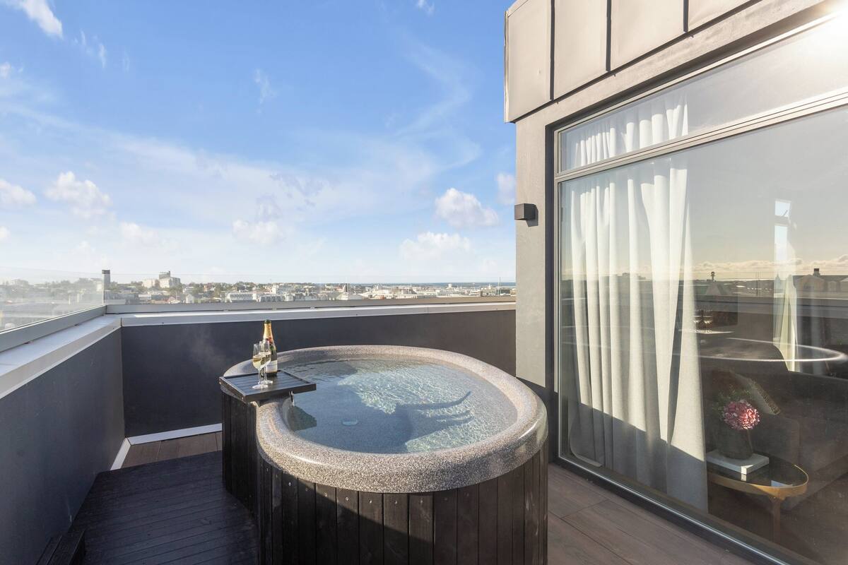 Een modern terras op het dak met een jacuzzi, een fles champagne en uitzicht op de stad.