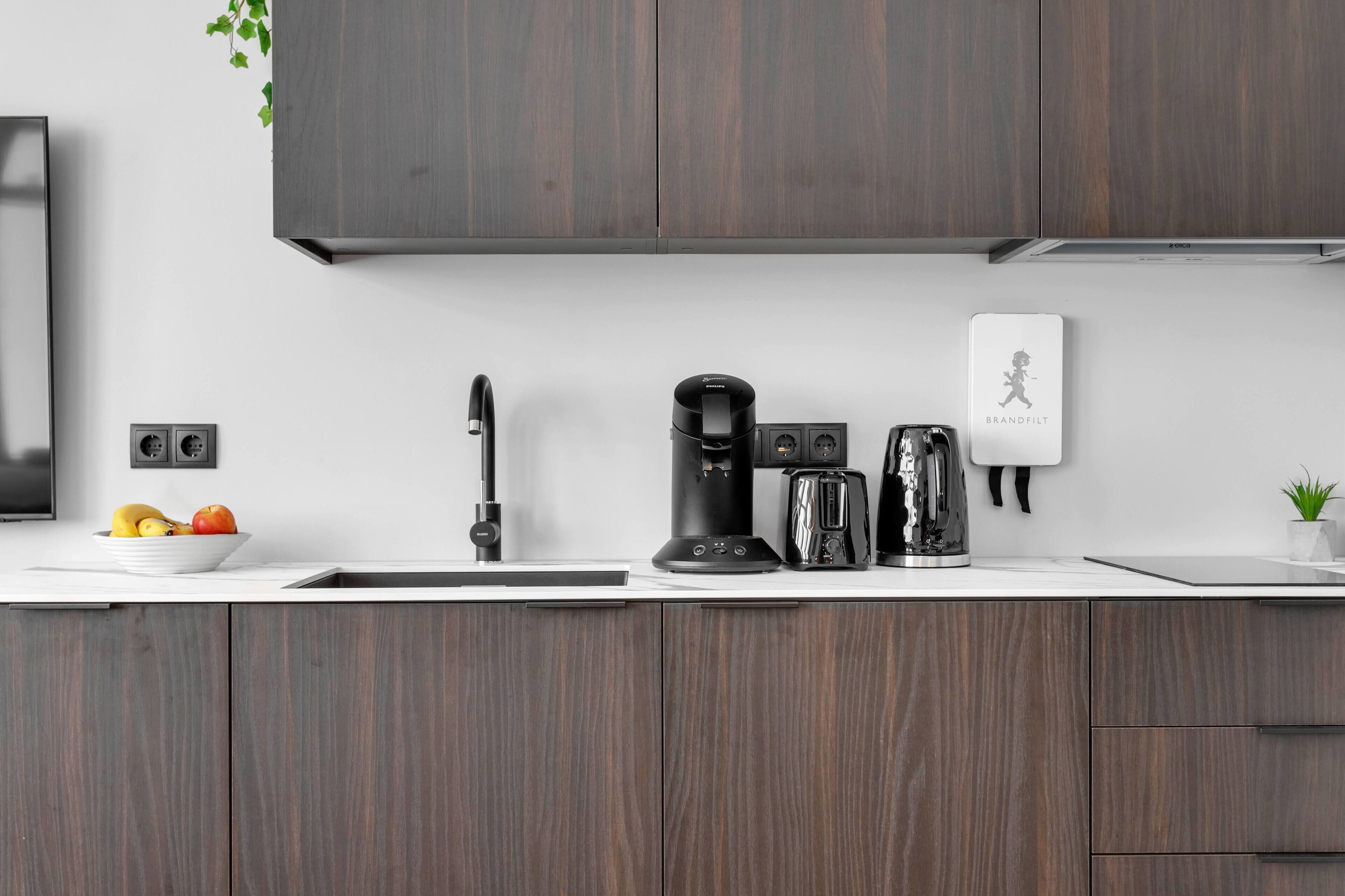 A modern kitchen with dark wood cabinets, a coffee maker, a toaster, and a small potted plant.