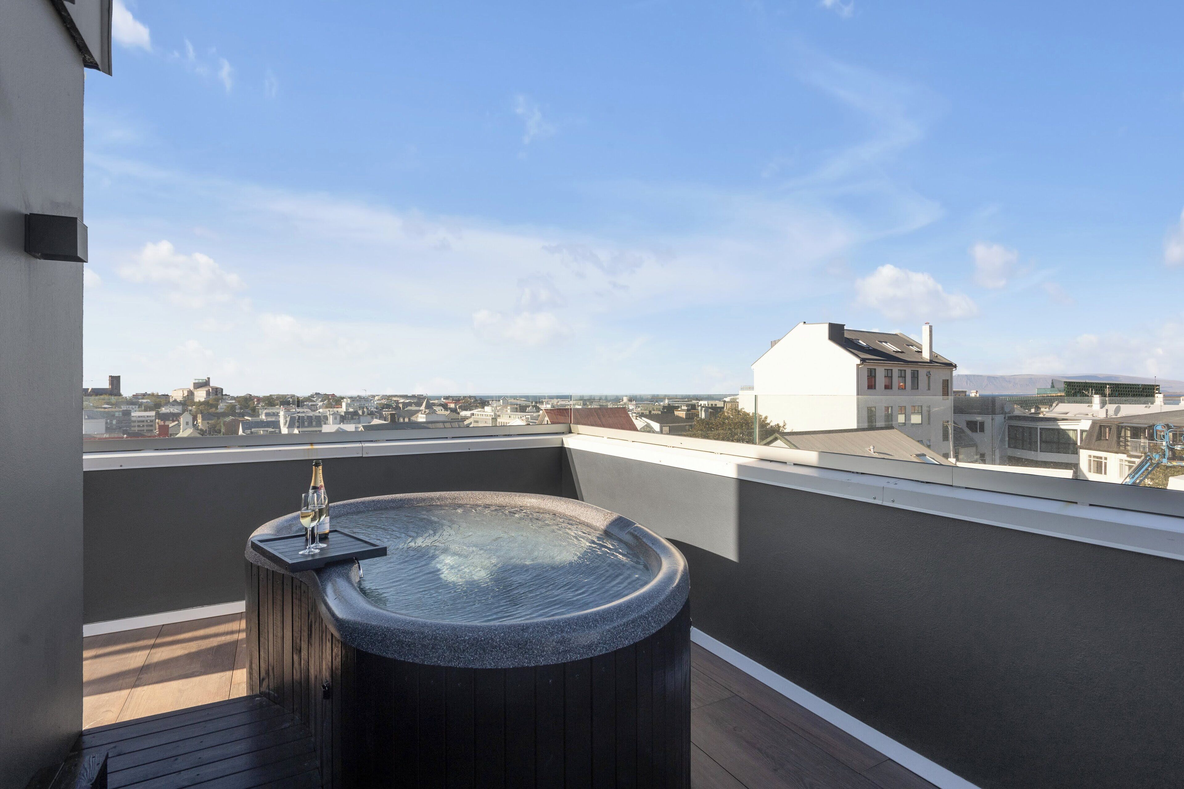 Une terrasse sur le toit avec un jacuzzi et une coupe de champagne, offrant une vue panoramique sur la ville.