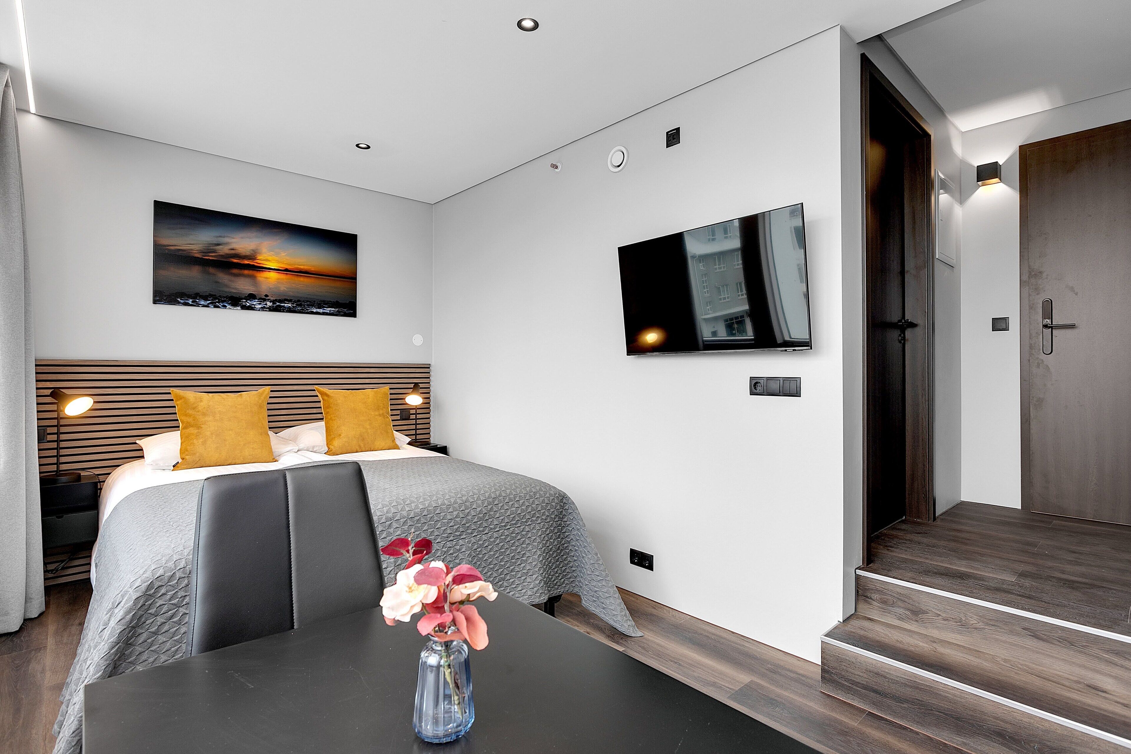 Une chambre d’hôtel moderne équipée d’un lit, d’un téléviseur à écran plat, d’un tableau et d’un vase avec des fleurs.