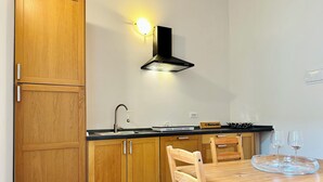 Une cuisine avec des meubles de rangement en bois, une hotte noire, un évier et une table à manger avec deux chaises.