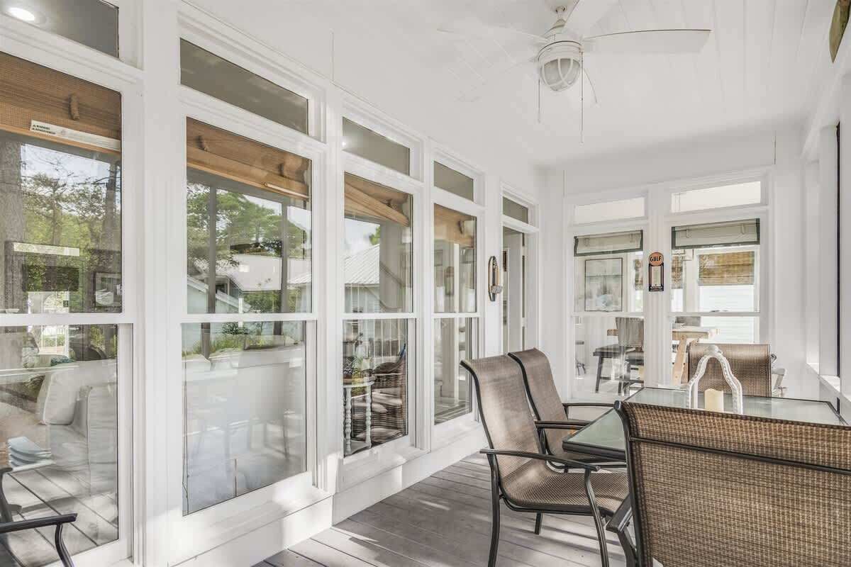 A sunroom with large windows, a glass table, wicker chairs, and a ceiling fan.
