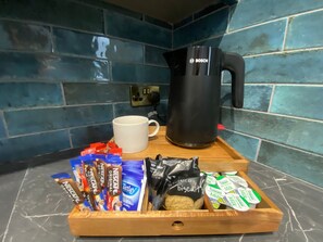 A kitchen counter with a coffee maker, a mug, and a tray with food items including biscuits and coffee packets.
