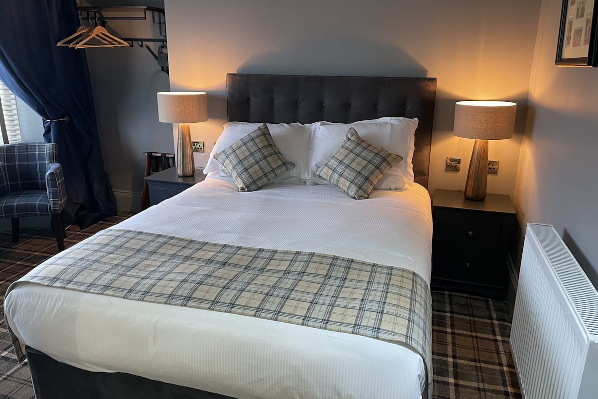 A neatly made bed with a plaid bedspread, two bedside lamps, and a headboard.
