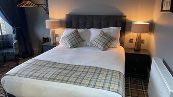 Een keurig opgemaakt bed met een geruite plaid, twee bedlampen en een hoofdbord.