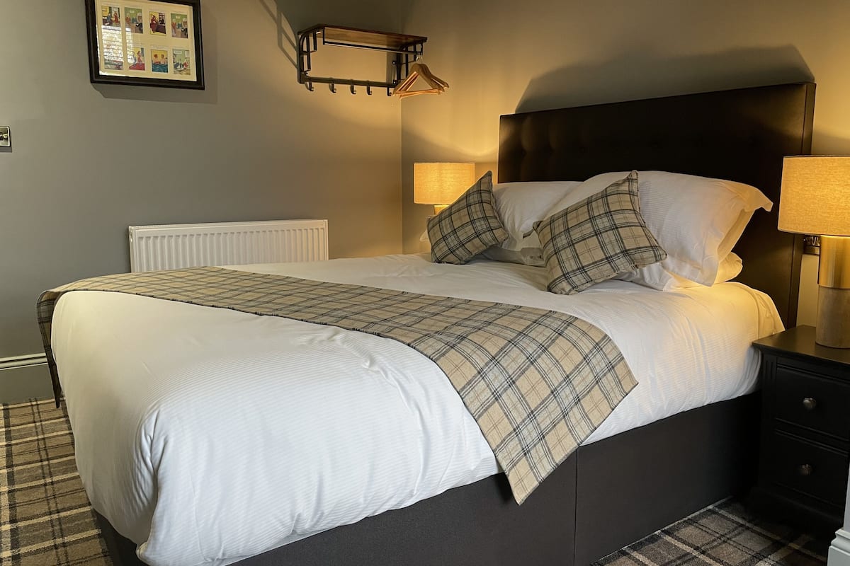 A neatly made bed with a plaid blanket, two bedside lamps, and a framed picture on the wall.