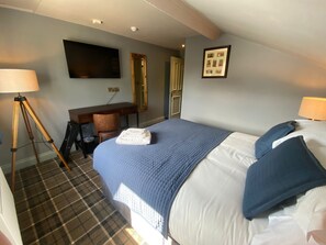 A hotel room with a bed, a desk, a chair, a lamp, a mirror, and a framed picture on the wall.