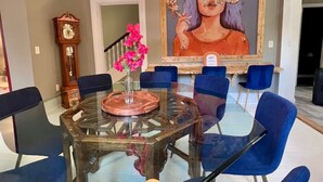A dining area with a glass table surrounded by blue chairs, a clock, and a painting on the wall. - The Hotel Avondale: 7b - 4bath + Skoolie tiny home (Birmingham)