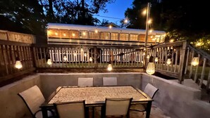 An outdoor patio with a table and chairs, surrounded by a wooden fence and string lights. - The Hotel Avondale: 7b - 4bath + Skoolie tiny home (Birmingham)