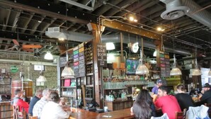 A bar area with wooden bar counters, hanging lights, and patrons seated at tables. - The Hotel Avondale: 7b - 4bath + Skoolie tiny home (Birmingham)