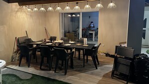 Un espace extérieur aménagé pour les repas, avec une table dressée pour quatre personnes, entourée de chaises. Une porte vitrée donne accès à une salle à manger.