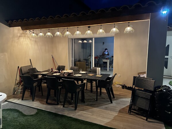 An outdoor dining area with a table set for four, surrounded by chairs. There is a glass door leading to a dining room. - Villa Famille 4 Chambres 10 Places (Chandolas)