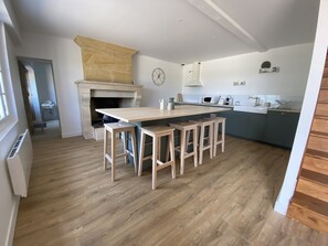 Een moderne keuken met een centraal eiland, houten krukken, een inbouwoven en een stenen open haard.