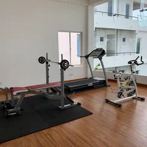 Un gimnasio con cinta de correr, bicicleta estática y banco para pesas.