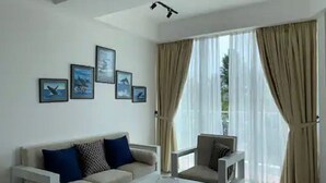 A modern living room with a sofa, armchair, and coffee table. There are framed pictures on the wall and a large window with curtains. - "Beach Haven Nilaveli" a home away from home (Nilaveli, Eastern Province, Sri Lanka)