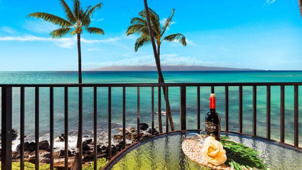 Une vue sur une plage tropicale, avec une table en verre, une bouteille de vin Cline et une fleur.