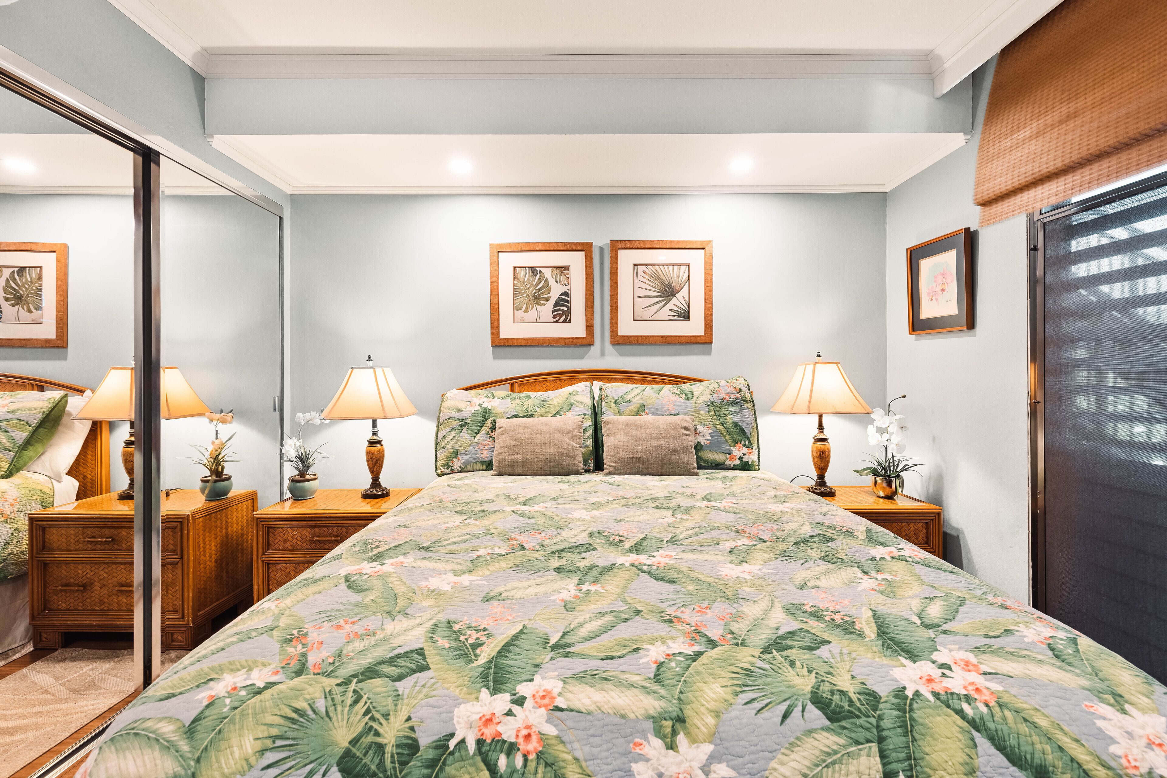 Une chambre à coucher avec un lit, deux tables de chevet avec des lampes, un miroir et des œuvres d’art encadrées accrochées au mur.