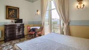 Een hotelkamer met een bed, een dressoir, een bureau met stoel, een schilderij aan de muur en een raam met gordijnen.