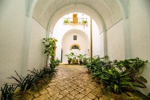 A narrow, arched corridor with a tiled floor, flanked by potted plants and a balcony with plants. - B&B A PALAZZO (Gagliano del Capo)