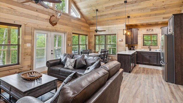 A spacious living room with a leather sofa, dining area, and kitchen with wooden walls and large windows. - *New Build* 3 BR w/ Hot Tub, Arcade, WiFi, Catch and Release Pond, Free Tickets (Sevierville)