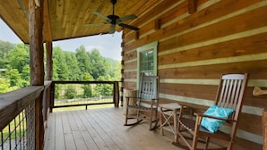 Une cabane en bois dotée d’un balcon, d’une chaise berçante et d’un fauteuil avec un coussin.