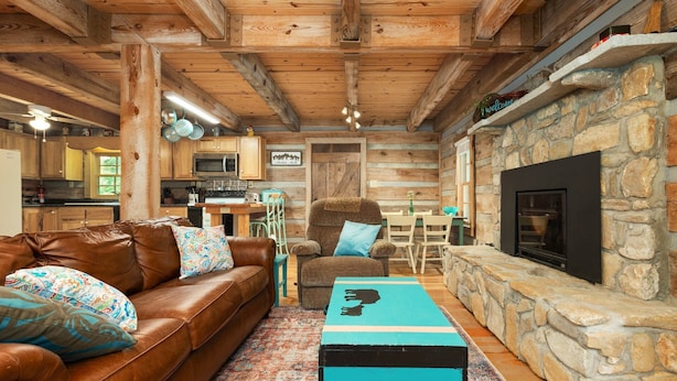 Un intérieur de chalet chaleureux avec une cheminée en pierre, des poutres en bois, un canapé en cuir et un coin repas.
