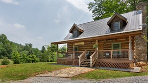 Une cabane en rondins avec des fondations en pierre, une véranda dotée d’une balustrade en bois et un escalier menant à l’entrée.