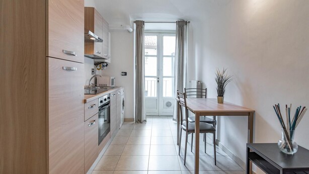A compact kitchen with wooden cabinets, a dining table with chairs, and a small potted plant. - Corte d Appello Rooms (Turin)