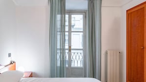 A bedroom with a bed, a wooden wardrobe, a radiator, and a window with curtains. - Corte d Appello Rooms (Turin)