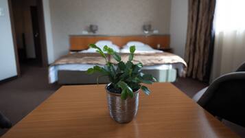 A hotel room with a wooden table, a potted plant, a bed with white linens, and a headboard.