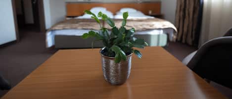 Una habitación de hotel con una mesa de madera, una planta en maceta, una cama con ropa blanca y un cabecero.