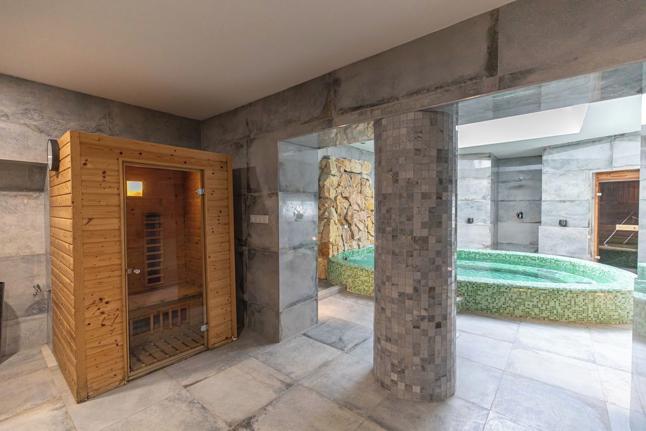 A modern spa area with a wooden sauna, a stone wall, and a mosaic-tiled pool.