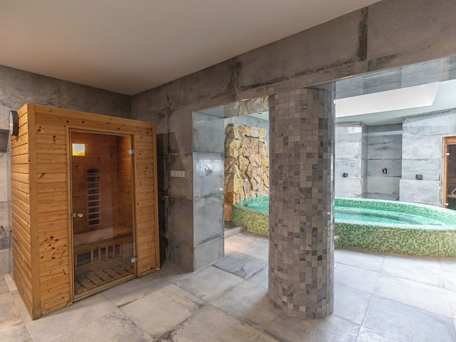 Un espace spa moderne doté d’un sauna en bois, d’un mur en pierre et d’une piscine dont le sol est recouvert de mosaïques.
