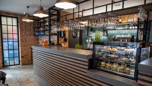 Zona de bar moderna con mostrador de madera, copas de vino colgantes y una vitrina con postres.