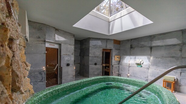 Un área de spa con una piscina de mosaico verde, paredes de piedra y un tragaluz.
