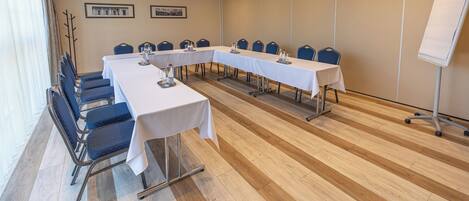 Un salón de conferencias con una larga mesa, sillas, una pizarra y cuadros en la pared.