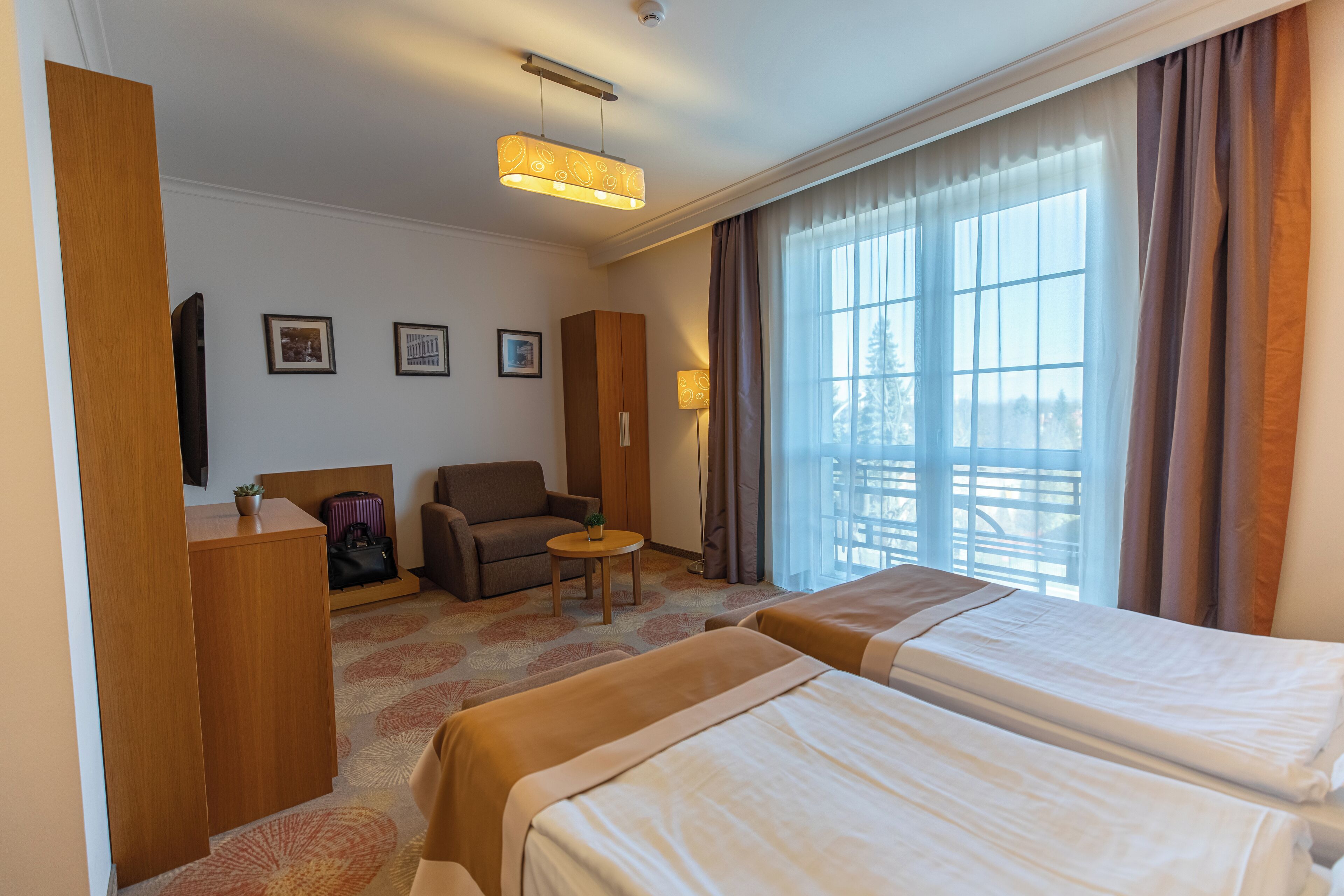 Habitación de hotel con dos camas, un escritorio, una silla, una mesita y un ventanal grande con cortinas.