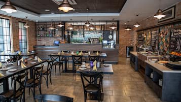 Un restaurante con paredes de ladrillo, iluminación colgante y una zona de bar. Las mesas están preparadas con platos y servilletas.