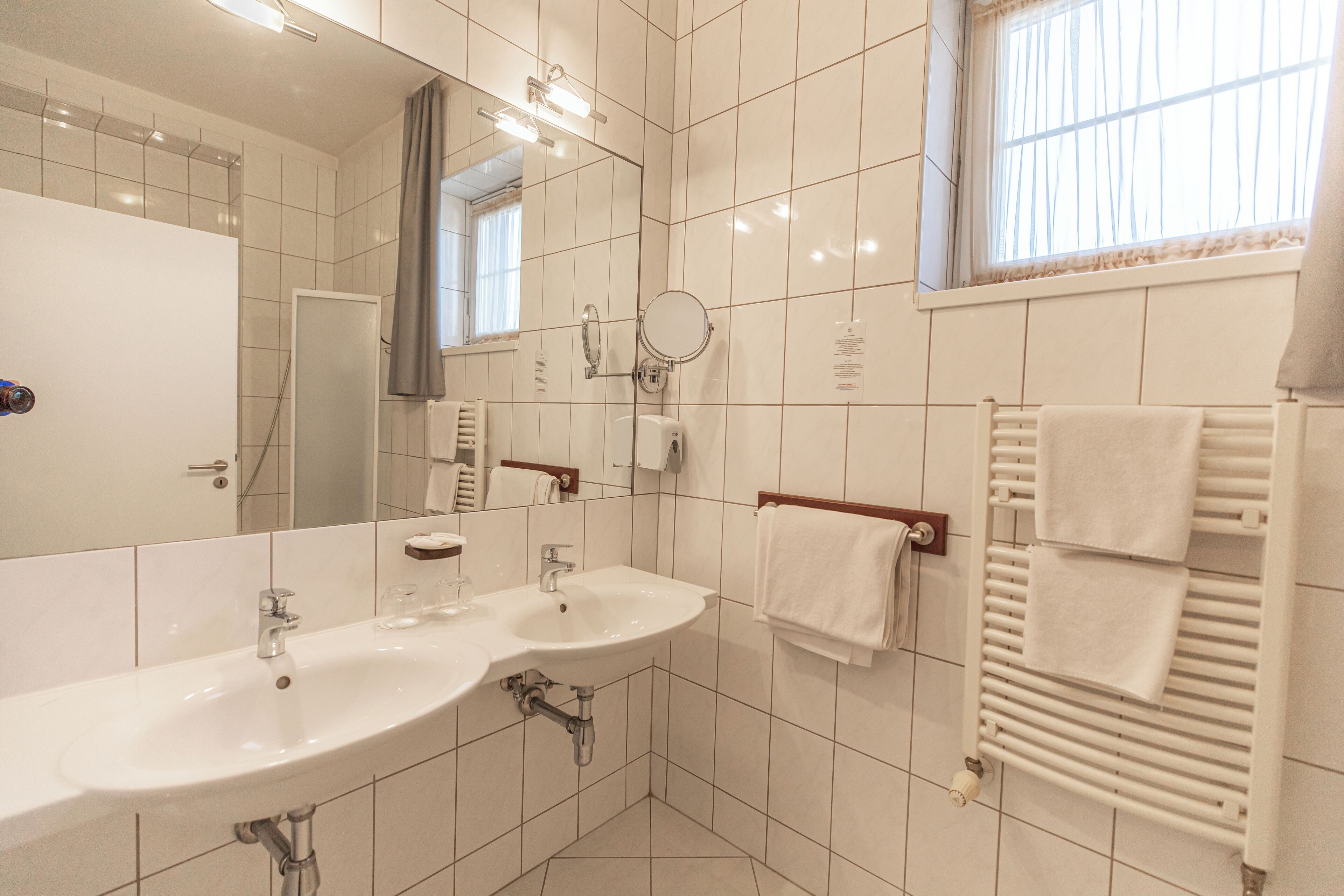 A modern bathroom with two sinks, a mirror, a towel rack, and a window with curtains.