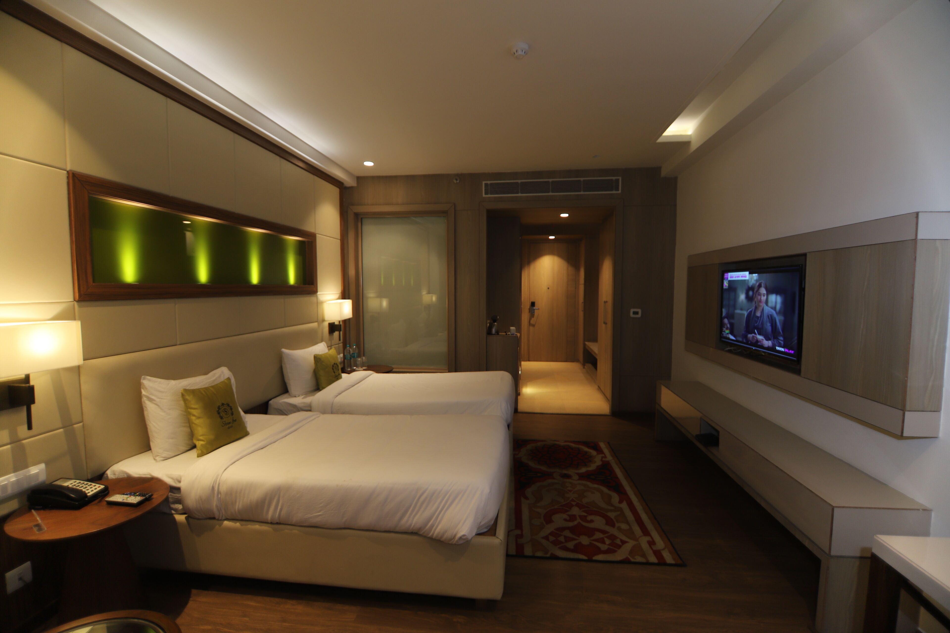 A hotel room with two beds, a TV, a desk, and a bathroom.