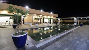 Un área de piscina nocturna con sillones de descanso y plantas en macetas.