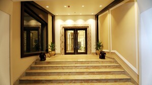Una imponente escalera conduce a una puerta doble, flanqueada por plantas en macetas y un espejo grande.